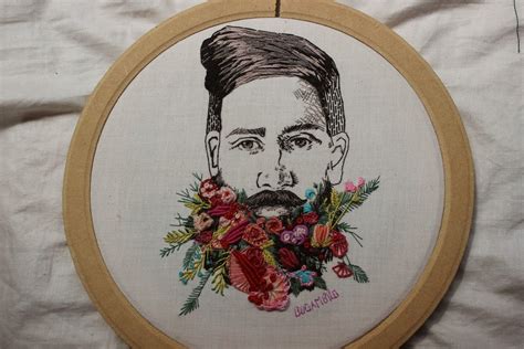 an embroidered portrait of a man with flowers in his beard is displayed on a white sheet