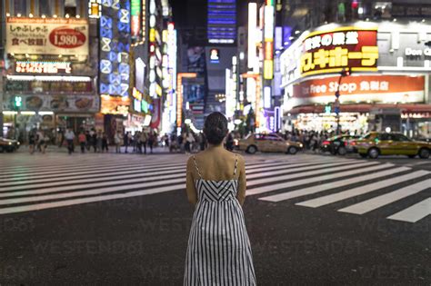 Young woman contemplating at night, people crossing Shinjuku Street ...