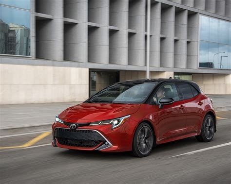 2021 Toyota Corolla Hatchback XSE Supersonic Red with black roof driving beside a big building ...