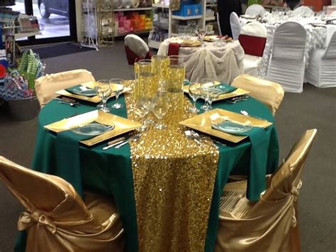 the table is set with gold and green cloths, silver place settings and napkins