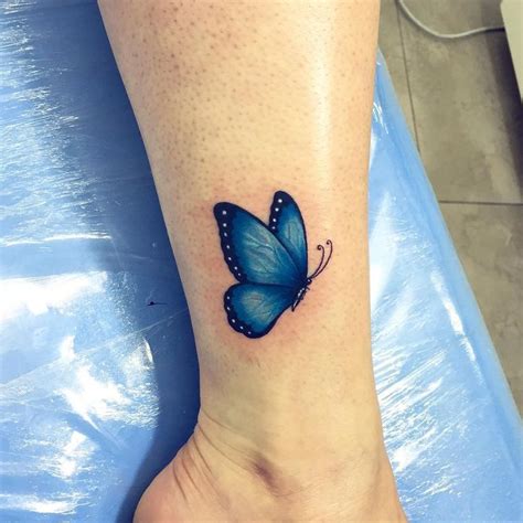 a small blue butterfly tattoo on the ankle, with text below it that reads tattoospenquenas