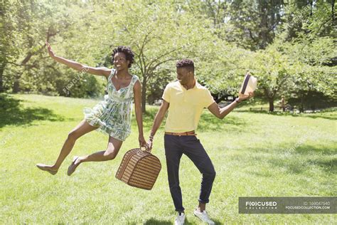 Young couple with picnic basket in park, with female jumping mid air — together, man - Stock ...