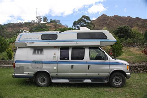 an rv parked in the grass with mountains in the background