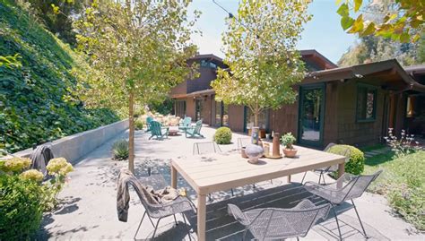 an outdoor patio with table and chairs in front of the house, surrounded by greenery