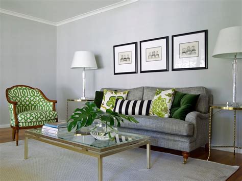 A series of patterned green pillows pop against the gray sofa and wall color. Glass lamps on ...