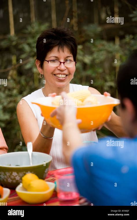 Mature woman passing a bowl of food at picnic table Stock Photo - Alamy