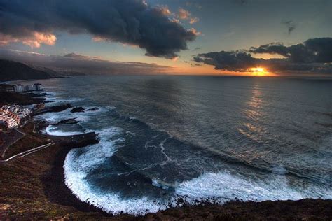 the sun is setting over the ocean with waves crashing in front of it ...