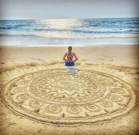 a woman sitting on the beach looking at an intricate design in the sand