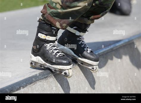 Feet of rollerblader wearing aggressive inline skates grinding on concrete ramp in outdoor skate ...