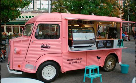 a pink food truck parked in front of a building next to a small blue stool