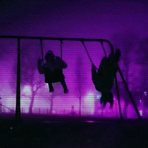 silhouettes of people on swings in front of purple light at night, with ...