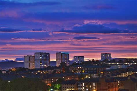 the city skyline is lit up at night with colorful clouds in the sky above it