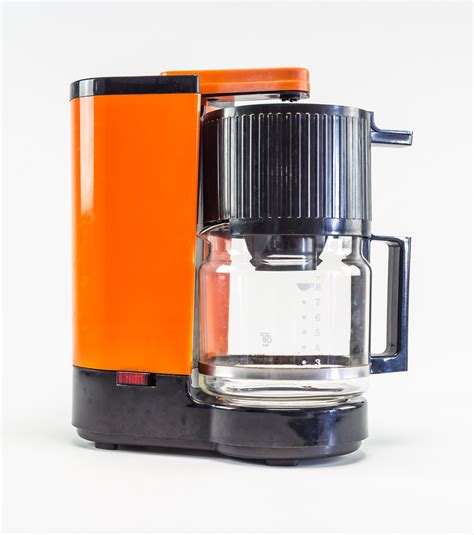 an orange and black coffee maker sitting on top of a white table next to a cup