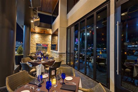 an outdoor dining area with tables and chairs at night time, overlooking the city lights