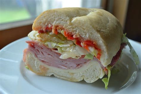 a sandwich with meat, cheese and lettuce sitting on a plate next to a window