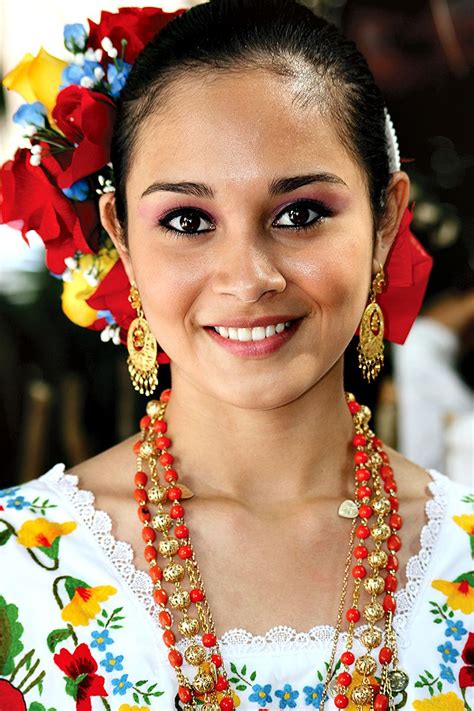 a woman in a colorful dress with necklaces and flowers on her head smiling at the camera