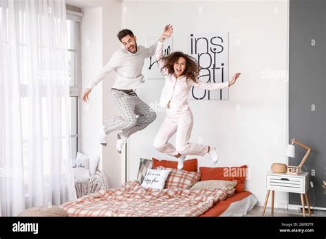 Happy young couple jumping on bed at home Stock Photo - Alamy