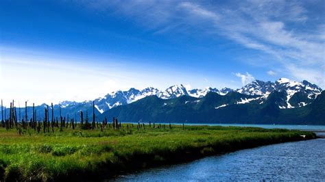 Landscape View Of Snow Covered Mountains River And Green Grass Field ...