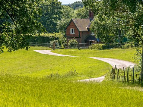 a house in the middle of a lush green field with a dirt road leading to it