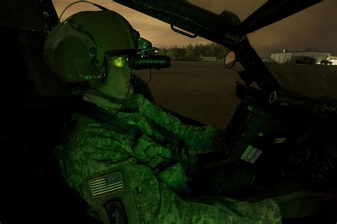 A pilot equipped with night vision goggles in the cockpit of an AH-64 ...