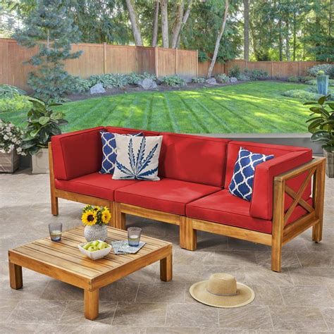 a red couch sitting on top of a patio next to a wooden coffee table with two blue and white pillows