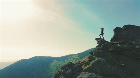 A man standing on top of a mountain with and raising his hands up the mountain. Victory and ...