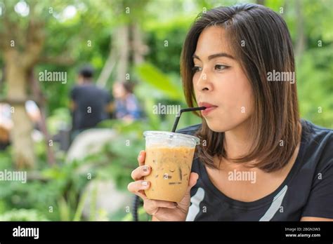 Asian woman holding a glass of cold espresso coffee Background blurry views tree Stock Photo - Alamy