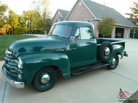 an old green truck parked in front of a house