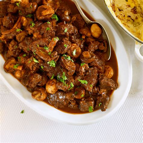 a white plate topped with meat and mushrooms next to a bowl of mashed potatoes