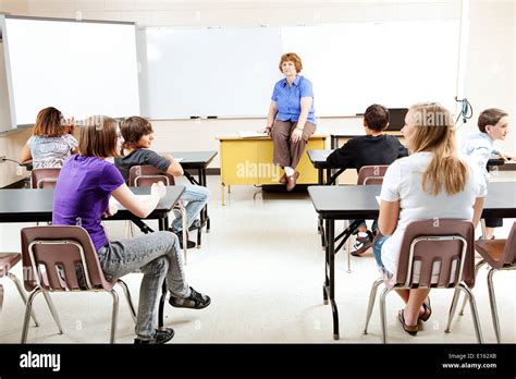 Teacher sitting on her desk, teaching a class of teenage students Stock Photo - Alamy