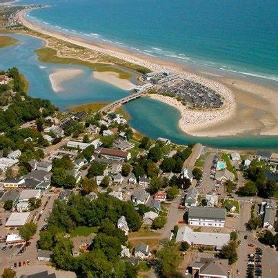 an aerial view of a town by the water and beach with houses, trees, and sand