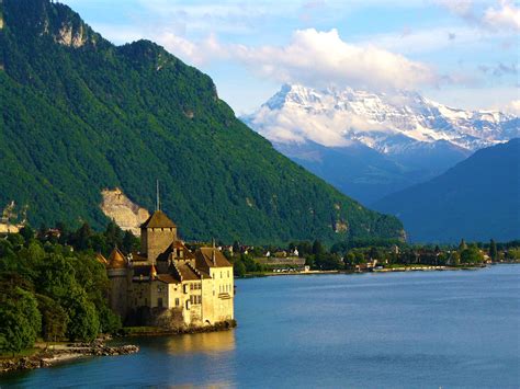 an old castle sits on the edge of a lake with mountains in the back ground