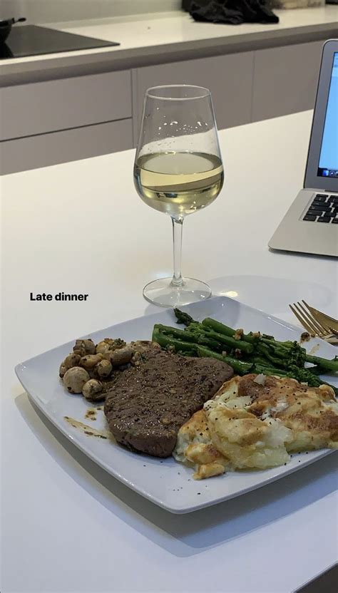 a white plate topped with meat and veggies next to a glass of wine