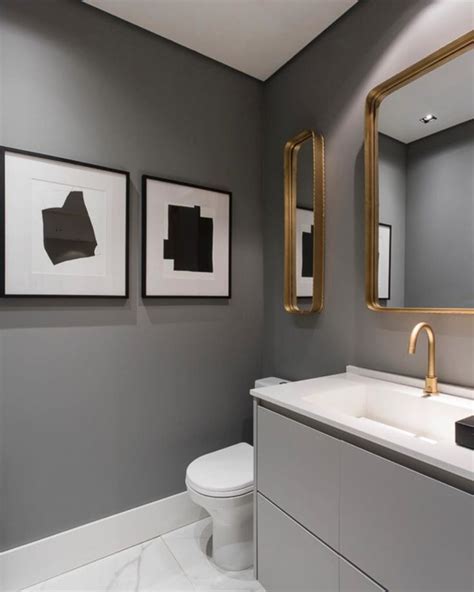 a bathroom with grey walls and gold framed pictures on the wall above the sink, along with a ...