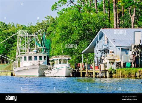 An oyster boat and shrimp boat are docked in front of a home on Fowl River, July 6, 2019, in ...