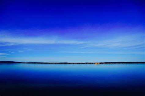 a deep blue lake and clear sky separated by a dark green shoreline on the horizon, blue lake ...