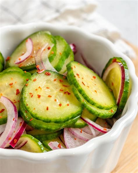 a white bowl filled with sliced cucumbers and red onions on top of a wooden table