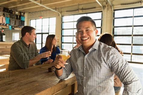 Portrait of smiling man drinking beer with friends in brew pub - Stock ...