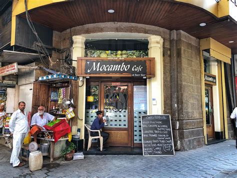 people are sitting at tables in front of a restaurant on the street ...