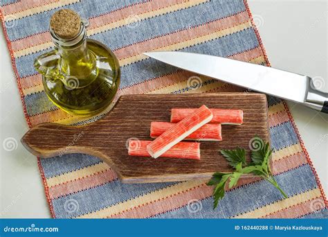 Surimi Crab Sticks and Parsley on a Brown Cutting Board Near Jar with Olive Oil and Sharp Chef ...