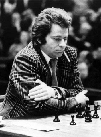a man sitting at a chess table with his arms crossed and looking down as he plays the game