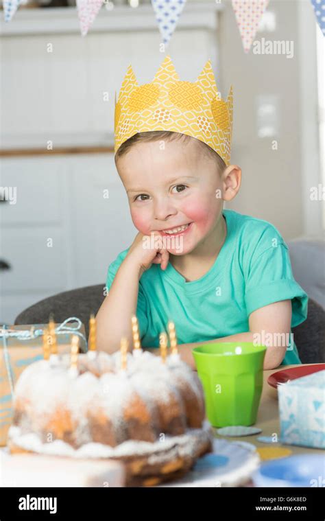 Happy boy wearing paper crown sitting at birthday table Stock Photo - Alamy