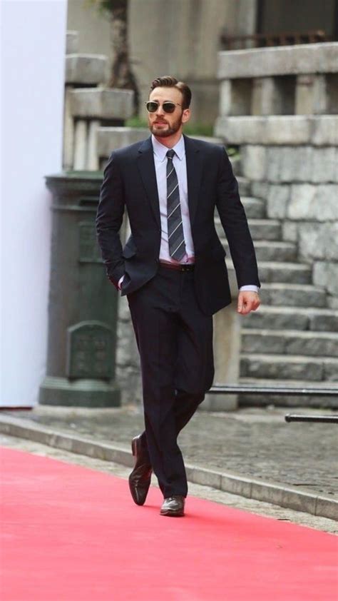 a man in a suit and tie is walking down the red carpeted area outside