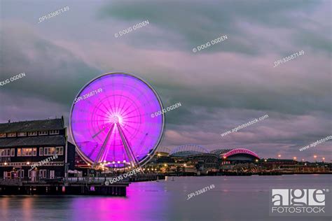 A cloudy evening on the Seattle waterfront looking at the Seattle Great Wheel reflecting off ...