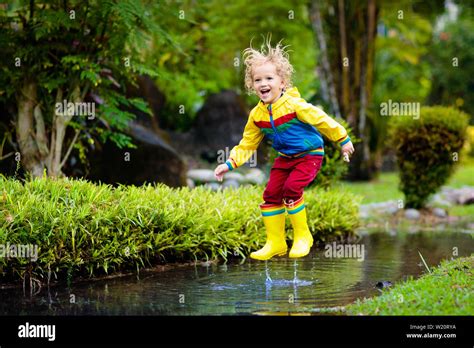 Child playing in puddle. Kids play and jump outdoor by autumn rain ...