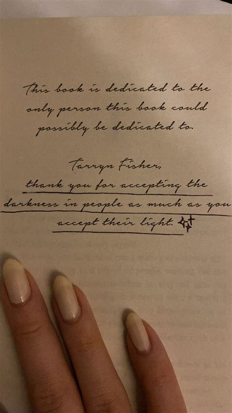 a woman's hand holding an open book with writing on the page next to her