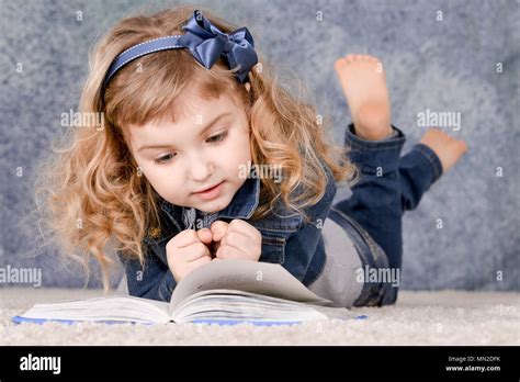 Cute little girl reading book while lying on floor Stock Photo - Alamy