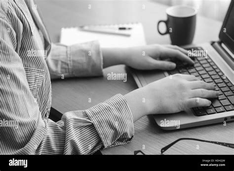 Female hands working at a laptop, black and white image. Coffee cup, notebook, pen, pencil ...