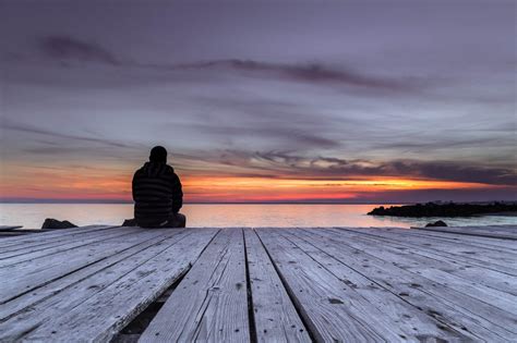 Man sitting on the pier and watching the sunset - The Thayer Institute