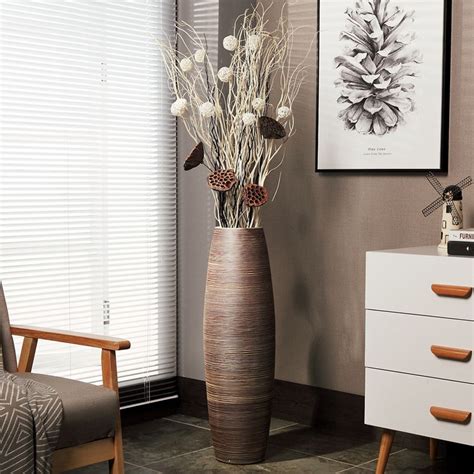 a tall vase with flowers in it next to a chair and pictures on the wall